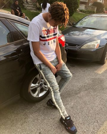The white t-shirt, black and red tommy jeans worn by YBN Cordae account on the Instagram of @ybncordae