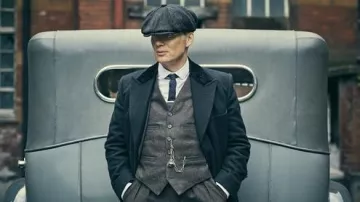 The navy blue overcoat with fur worn by Thomas Shelby (Cillian Murphy) in the series Peaky Blinders (Season 2 Episode 1)