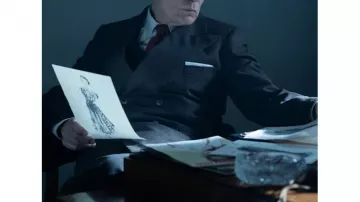 Les tenues de la série télévisée New Look : John Malkovich porte un costume gris foncé pour incarner Lucien Lelong dans la saison 1