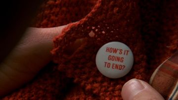 The badge "HOW'S IT GOING TO END?" worn by Lauren / Sylvia (Natascha McElhone) in The Truman Show movie