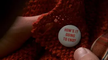 Le badge "HOW'S IT GOING TO END?" porté par Lauren / Sylvia (Na­tas­cha McEl­hone) dans le film The Truman Show