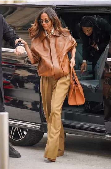 Blouson aviateur Saint Laurent en cuir d’agneau plongeant brillant porté par Zoé Saldana à Paris le 11 mars 2025