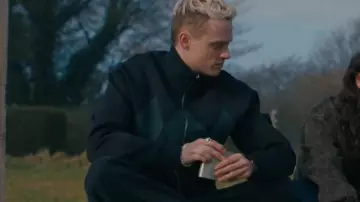 Cárdigan oscuro con cremallera y estampado de rombos verdes y cuello alto usado por Eddie Harrigan (Anson Boon) en MobLand (S01E07)