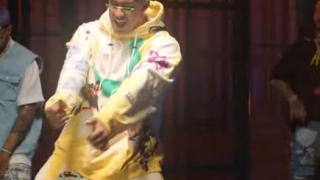 Le sweatshirt à capuche jaune 99%IS de Bad Bunny dans le clip No Me Conoce (Remix) de Jhay Cortez, J. Balvin, Bad Bunny