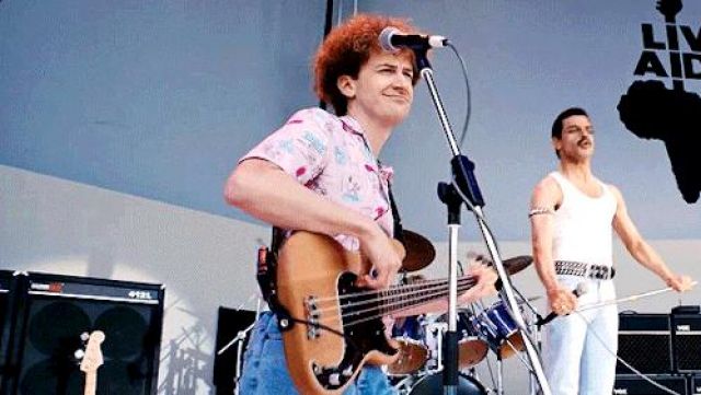 La chemise rose imprimée manches courtes de John Deacon (Joe Mazello) dans Bohemian Rhapsody