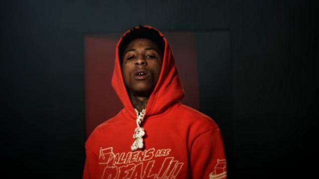 Merch Lyri­cal Lemon­ade Aliens Are Re­al Hood­ie in red worn by YoungBoy Never Broke Again in his AI Nash music video