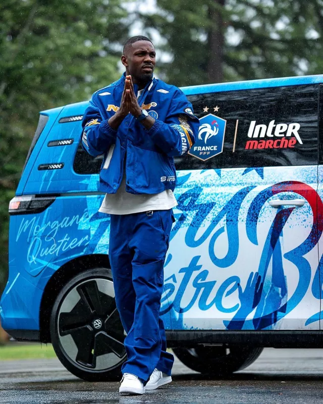 Marcus Thuram Wardrobe: Nike Nocta L'Art Deep Blue Carpenter Pants worn by him arriving at French Team Camp in Clairefontaine