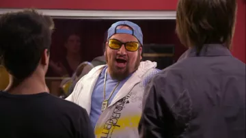 Tenues Big Time Rush : Gustavo Rocque (Stephen Kramer Glickman) porte un sweat à capuche zippé blanc avec des couleurs et des lettres noires dans la saison 1, épisode 15