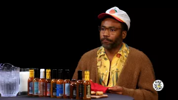 Donald Glover AKA Childish Gambino est une chemise imprimée jaune brûlante de Donald Glover dans Hot Ones en juillet 2024