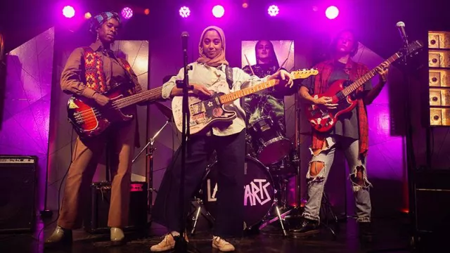Instrumentos musicales de We Are Lady Parts: Amina (Anjana Vasan) toca la guitarra eléctrica en el escenario en el episodio 1 de la temporada 2